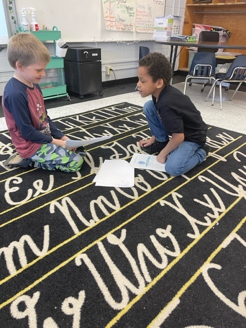 Two students reading to each other on rug
